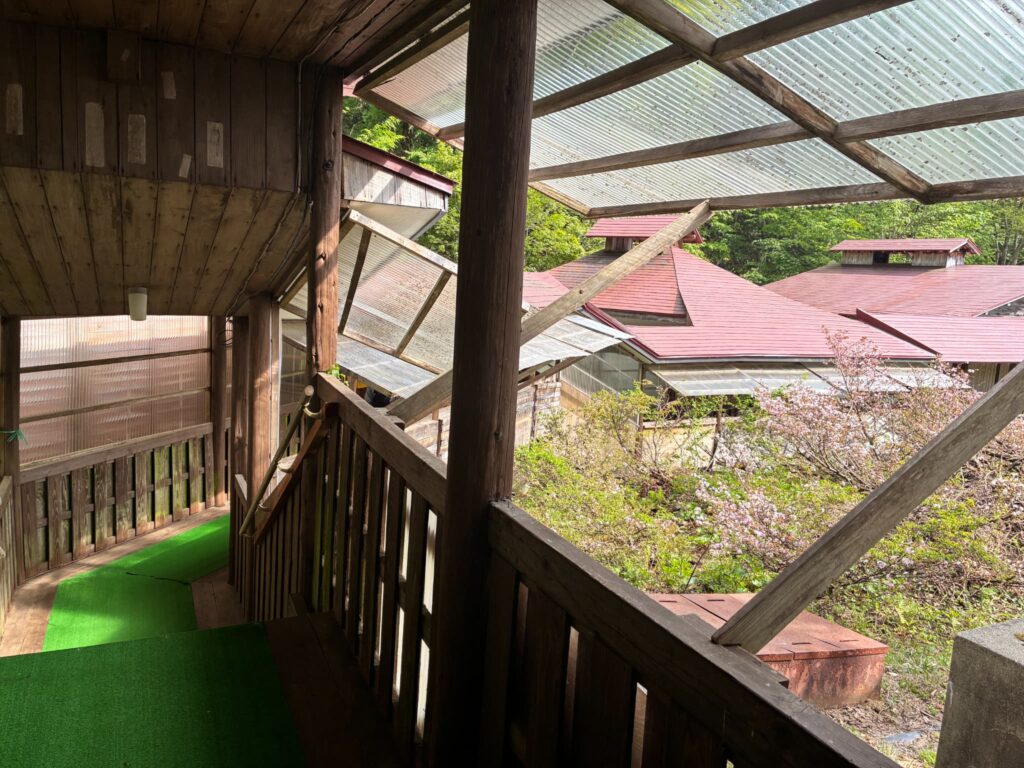 蟹場温泉の長い木造渡り廊下から見える赤い屋根の建物と新緑