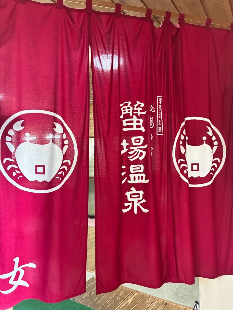 蟹場温泉のロゴと文字が白く染め抜かれた風情あるえんじ色の暖簾
